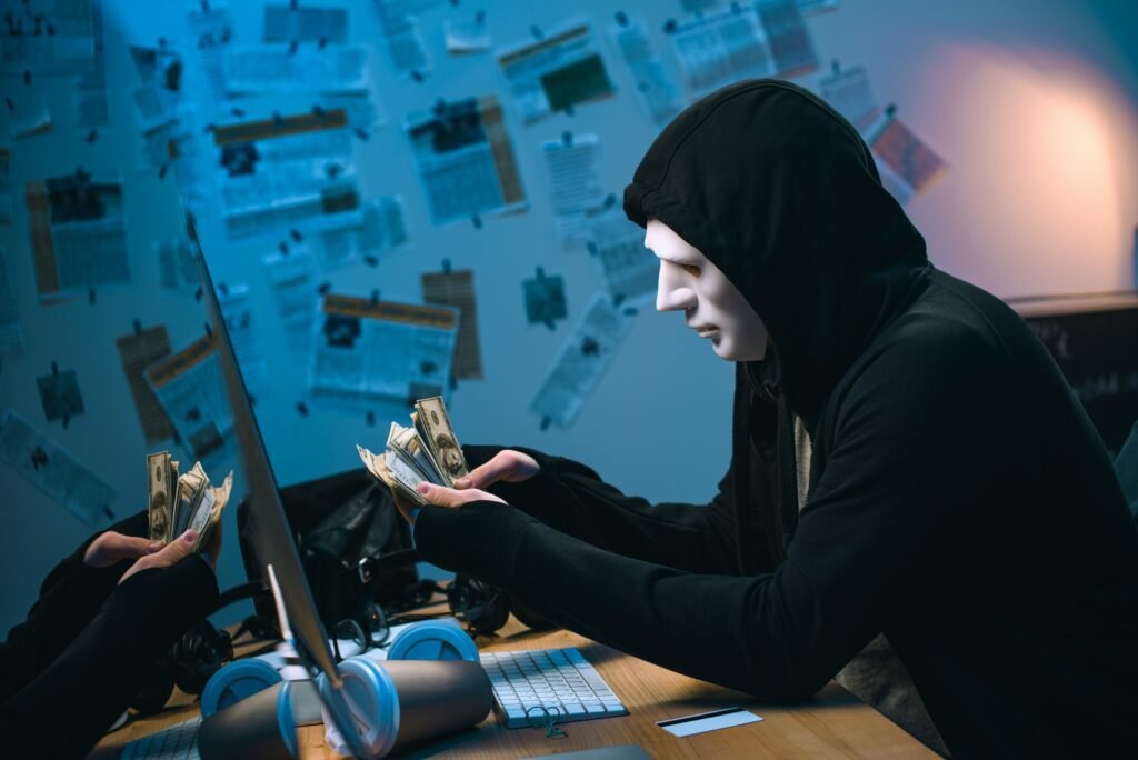 forex scams side view of hooded hacker in mask counting stolen money at his workplace